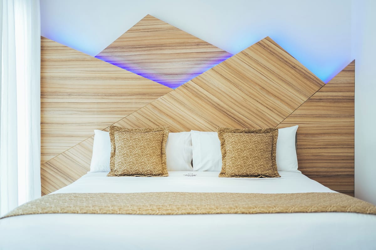 Quarto de hotel com cabeceira de madeira, roupa de cama branca e almofadas estampadas.