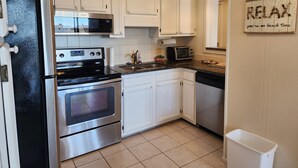 Una cocina con armarios blancos, un refrigerador de acero inoxidable, un microondas, un tostador y un lavabo.
