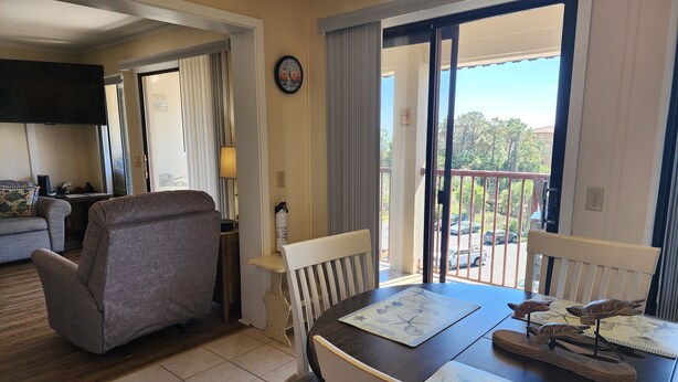 Habitación de hotel con una mesa de comedor, sillas, un sofá, un televisor y un balcón con vistas a la calle.
