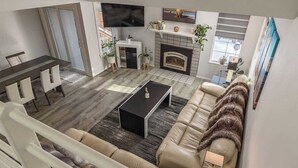 Ein modernes Wohnzimmer mit einer Couch, einem Couchtisch, einem Fernseher, einem Kamin und einem Essbereich.
