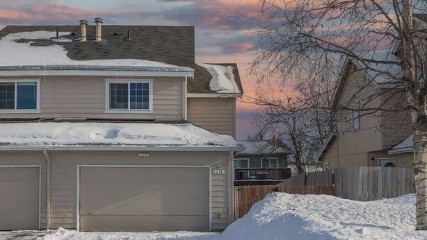 Una casa de dos pisos con un garaje, rodeada de nieve.