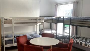 A dormitory room with bunk beds, a round table, and red chairs.