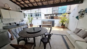 A patio area with a round table, chairs, a sofa, a kitchen area, and potted plants. - Fullano B&B (Rio de Janeiro)
