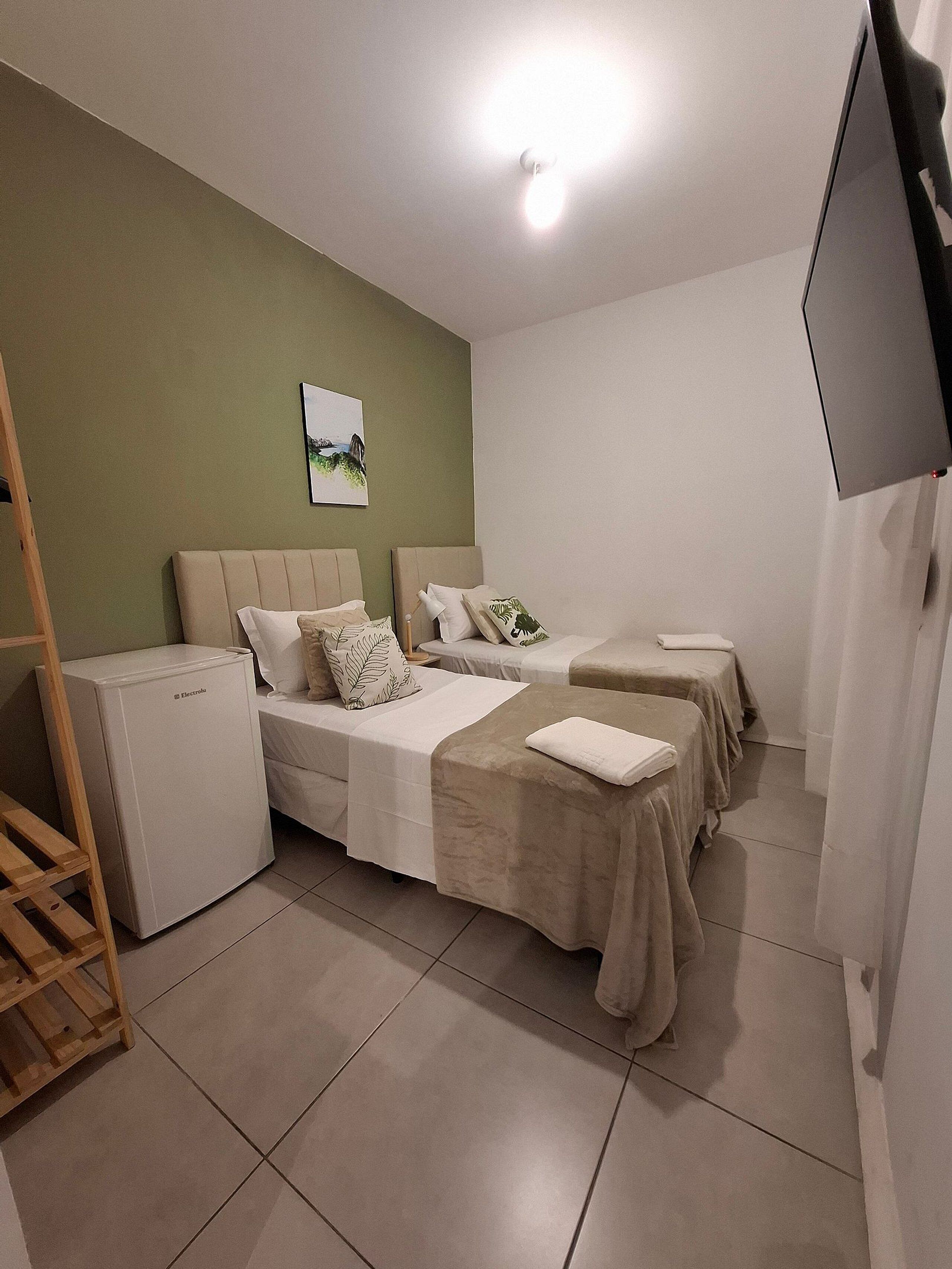 A hotel room with two beds, a small refrigerator, a wooden ladder, a flat-screen TV, and a painting on the wall.
