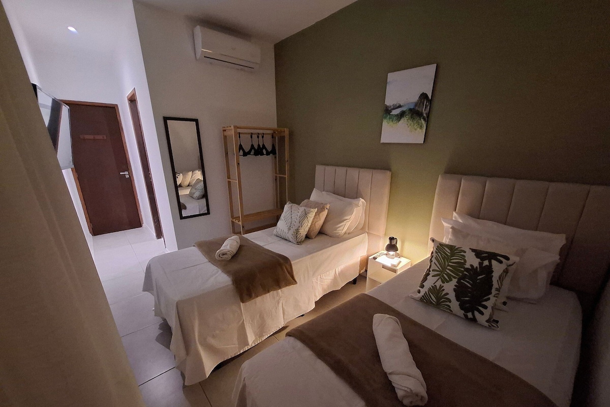 Habitación de hotel con dos camas, una mesita de noche con lámpara, un espejo y un cuadro en la pared.