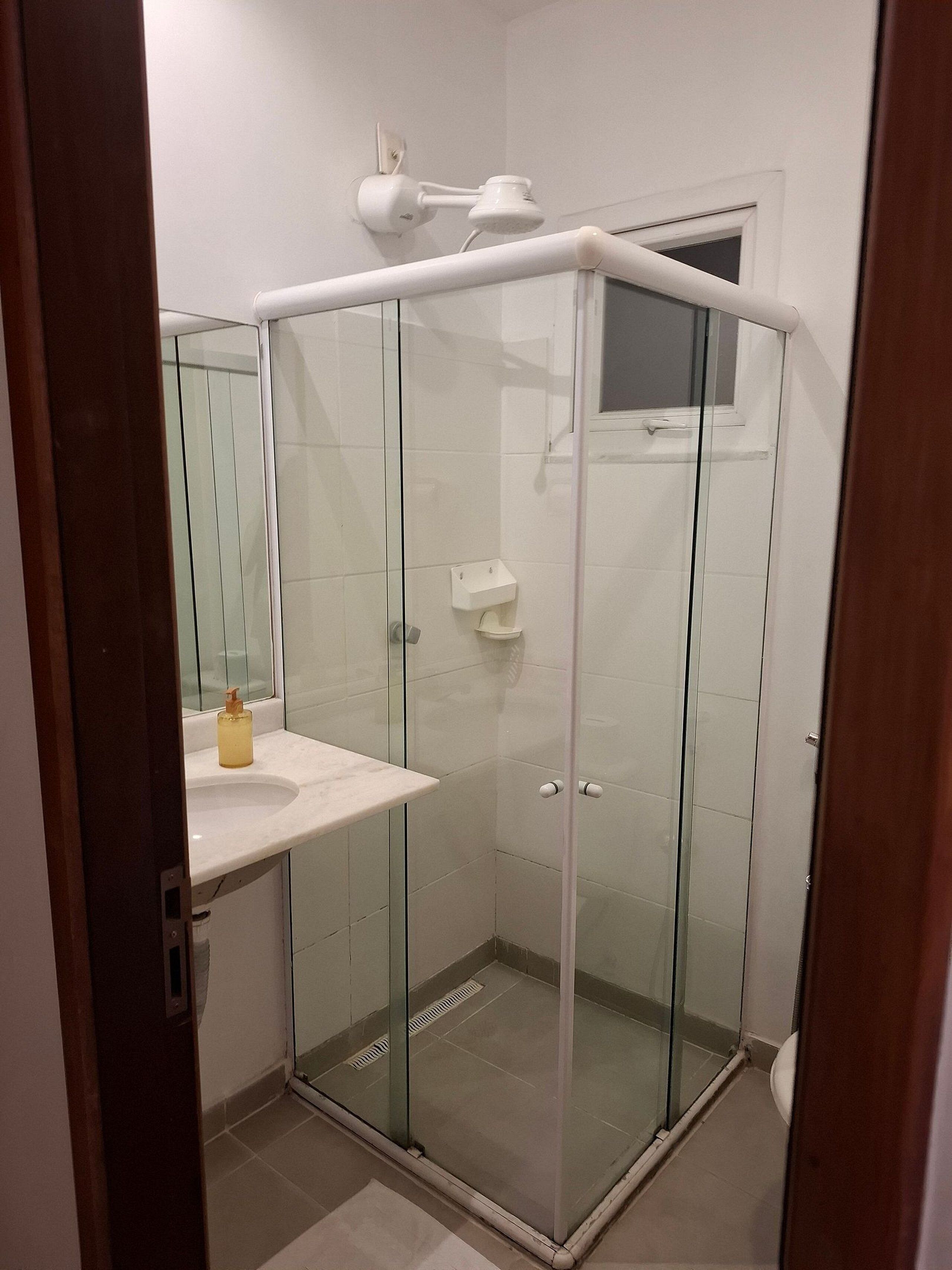 A glass-enclosed shower with a white sink and a small mirror.