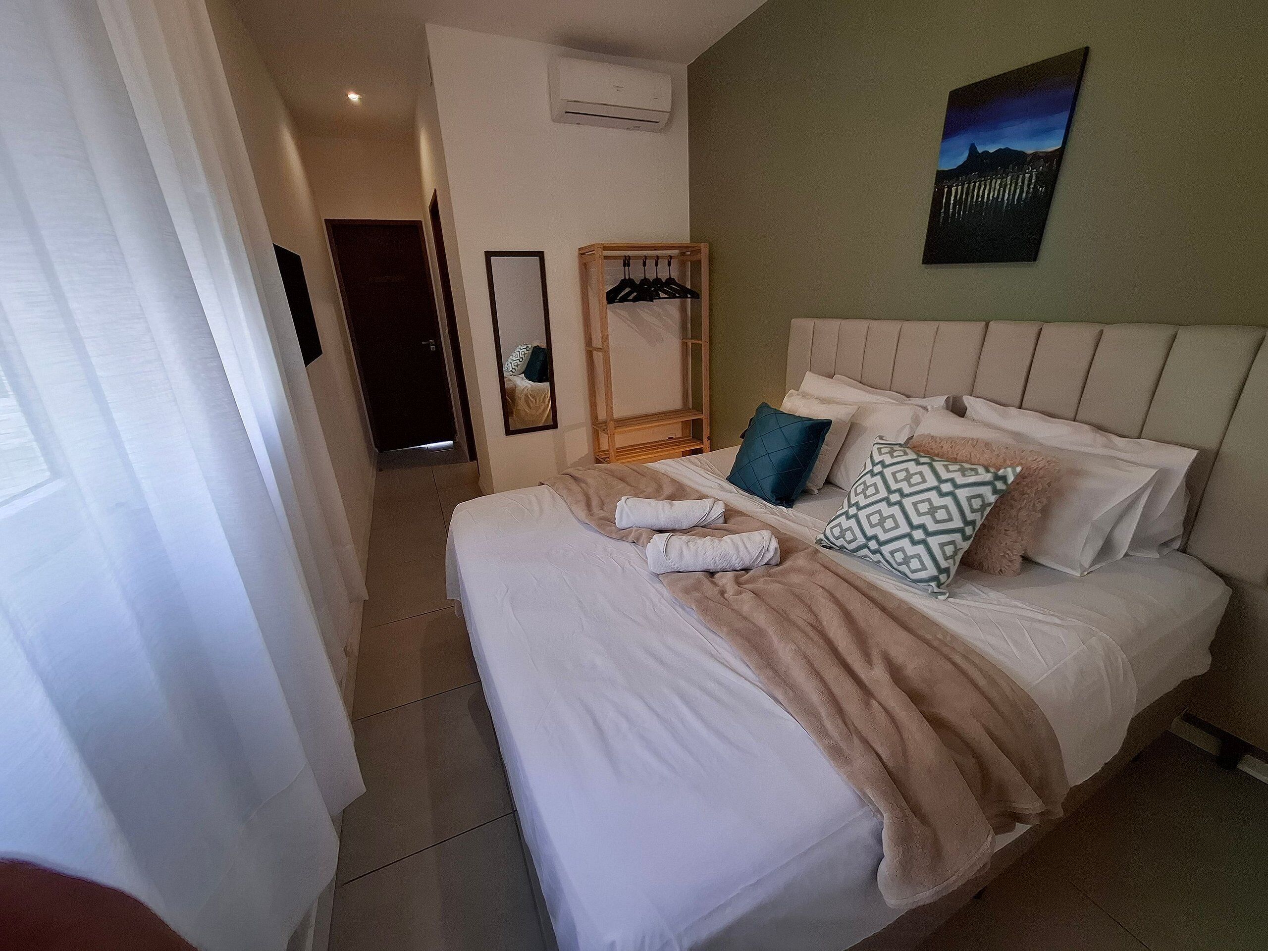 A hotel room with a bed, a mirror, a coat rack, and a painting on the wall.