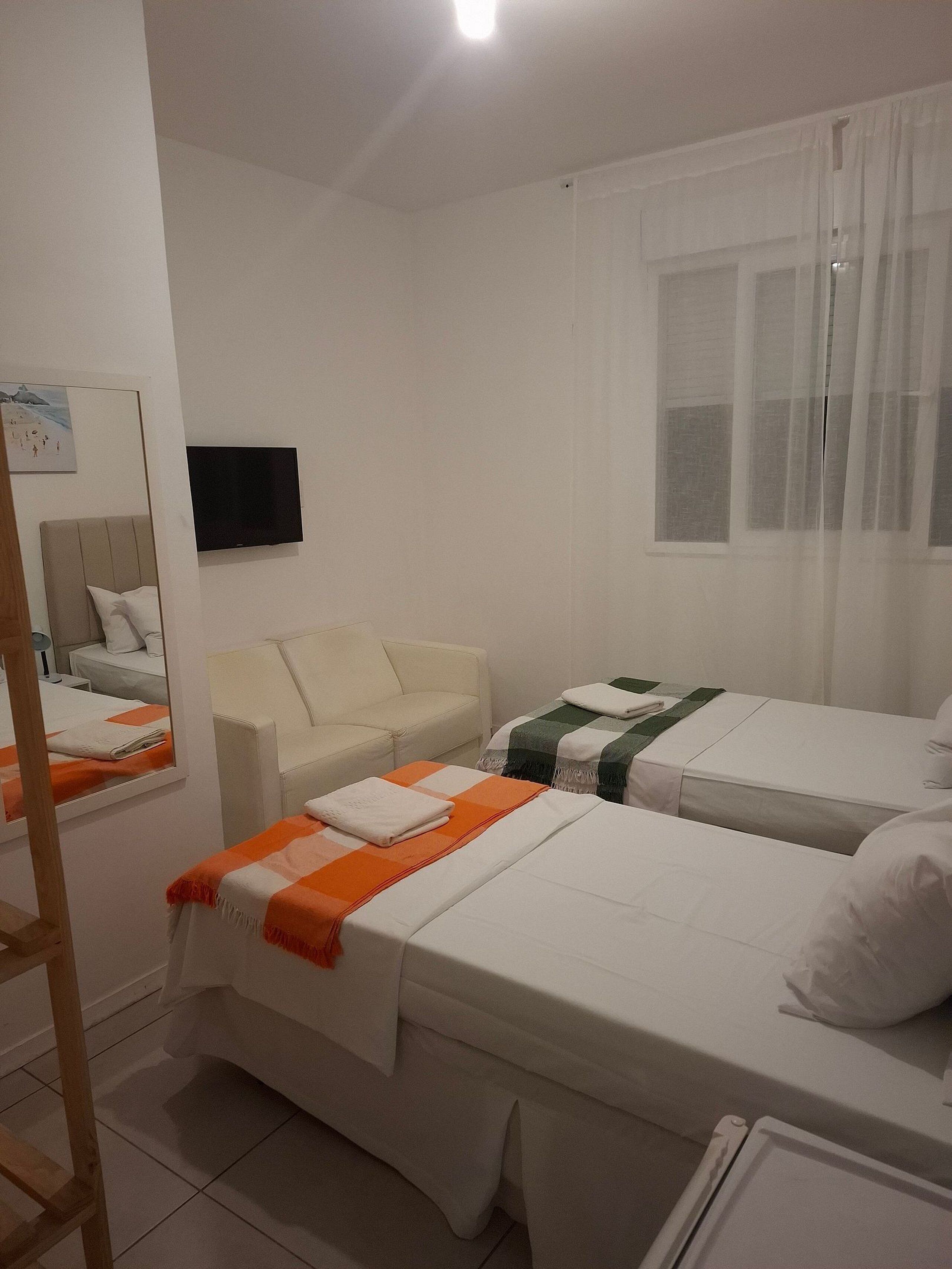 Hotellihuone, jossa on kaksi erillistä sänkyä, sohva, televisio ja ikkuna, jossa on verhot.