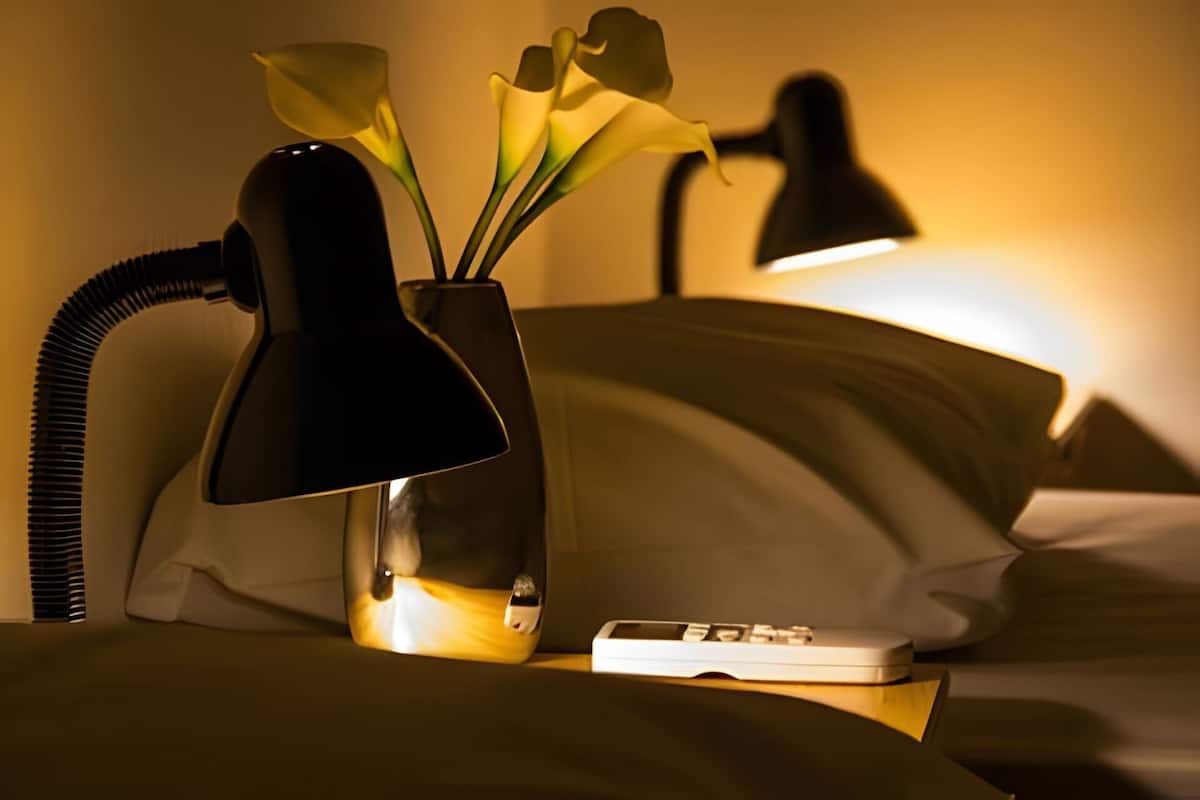 Una cama con una lámpara, un control remoto y un florero con flores.