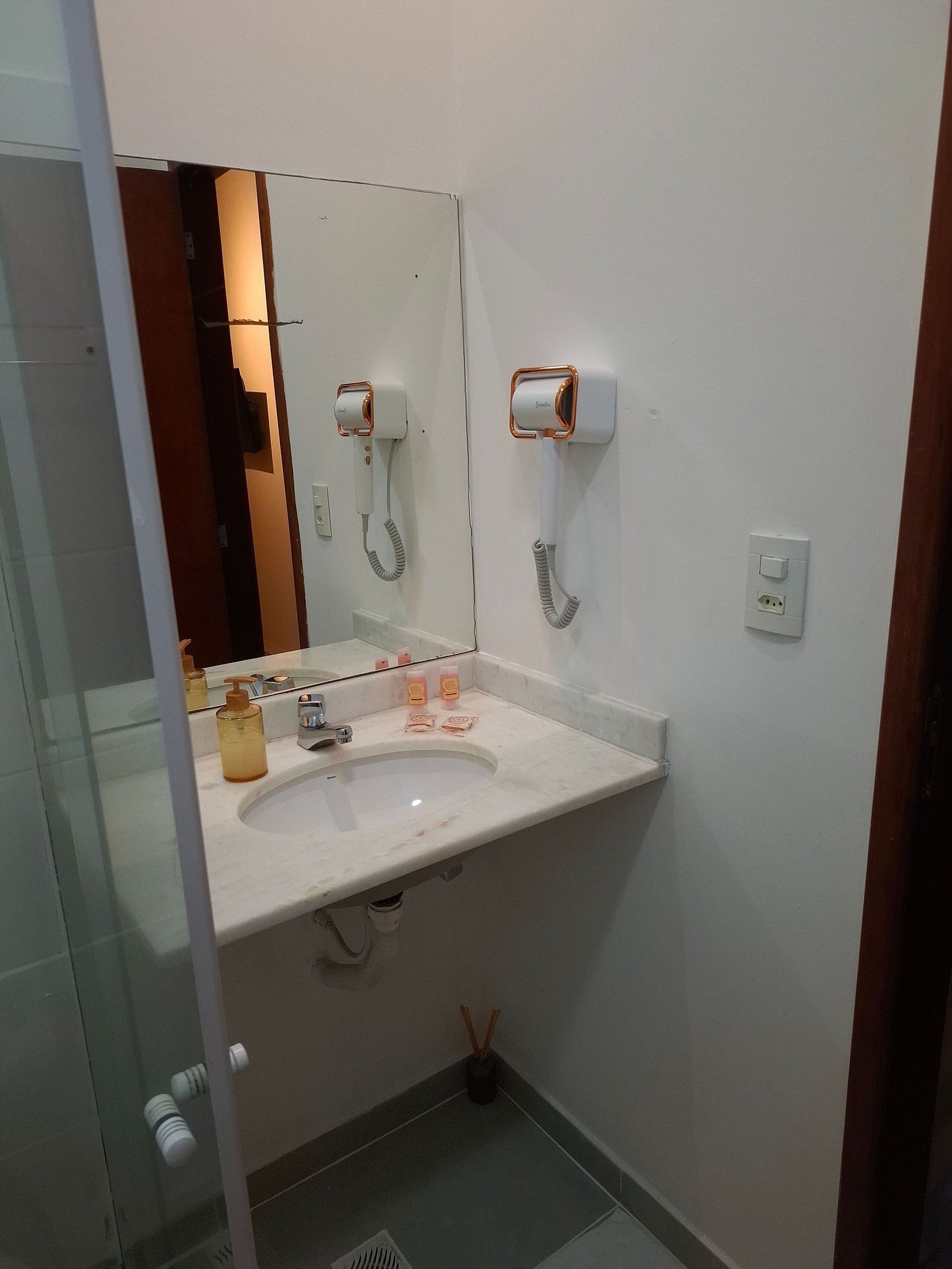 A bathroom with a white sink, a mirror, a hairdryer, and a soap dispenser.