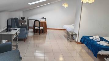 Una habitación amplia con techo alto, un comedor con mesa y sillas, una cama con una colcha azul, y un escritorio con una silla.