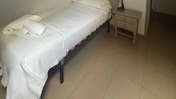 Uma cama de casal com roupa de cama branca, uma mesa de cabeceira com abajur e uma luminária na parede.
