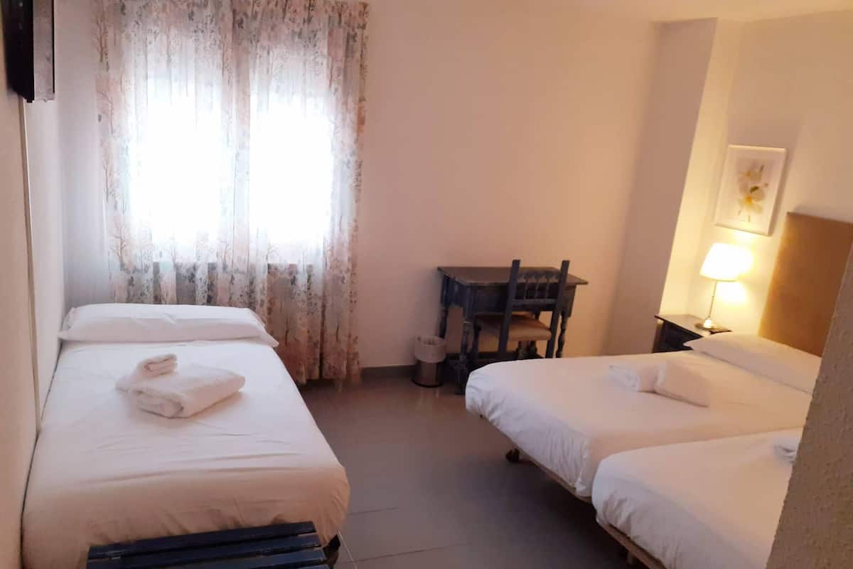 Ein Hotelzimmer mit zwei Einzelbetten, einer hölzernen Bank, einem kleinen Tisch, einem Stuhl und einer Lampe.