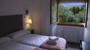 Une chambre avec deux lits, une table de chevet avec une lampe, une fenêtre donnant sur des arbres et un radiateur.