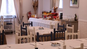 Un espace repas avec des tables dressées pour le repas, une table de buffet garnie de fruits et de boissons, et un extincteur fixé au mur.