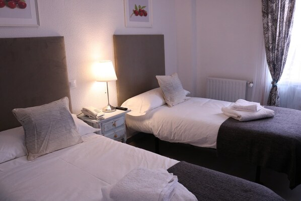 Une chambre d’hôtel avec deux lits, une table de chevet avec une lampe, un téléphone et une serviette pliée sur le sol.