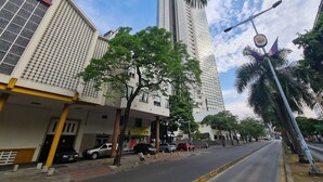 Vista da rua com edifícios altos, carros estacionados e céu claro.
