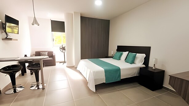 Quarto de hotel moderno com cama, escrivaninha, duas cadeiras, mesa de cabeceira e janela com cortinas.