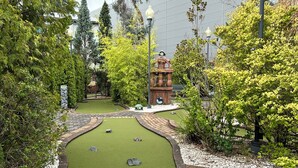 Ein Minigolfplatz mit einem gewundenen Weg, grünem Kunstrasen und dekorativen Elementen wie einer Statue und einem Brunnen.