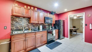 Una cocina con armarios de madera, encimera negra, salpicadero de azulejos y refrigerador de acero inoxidable.
