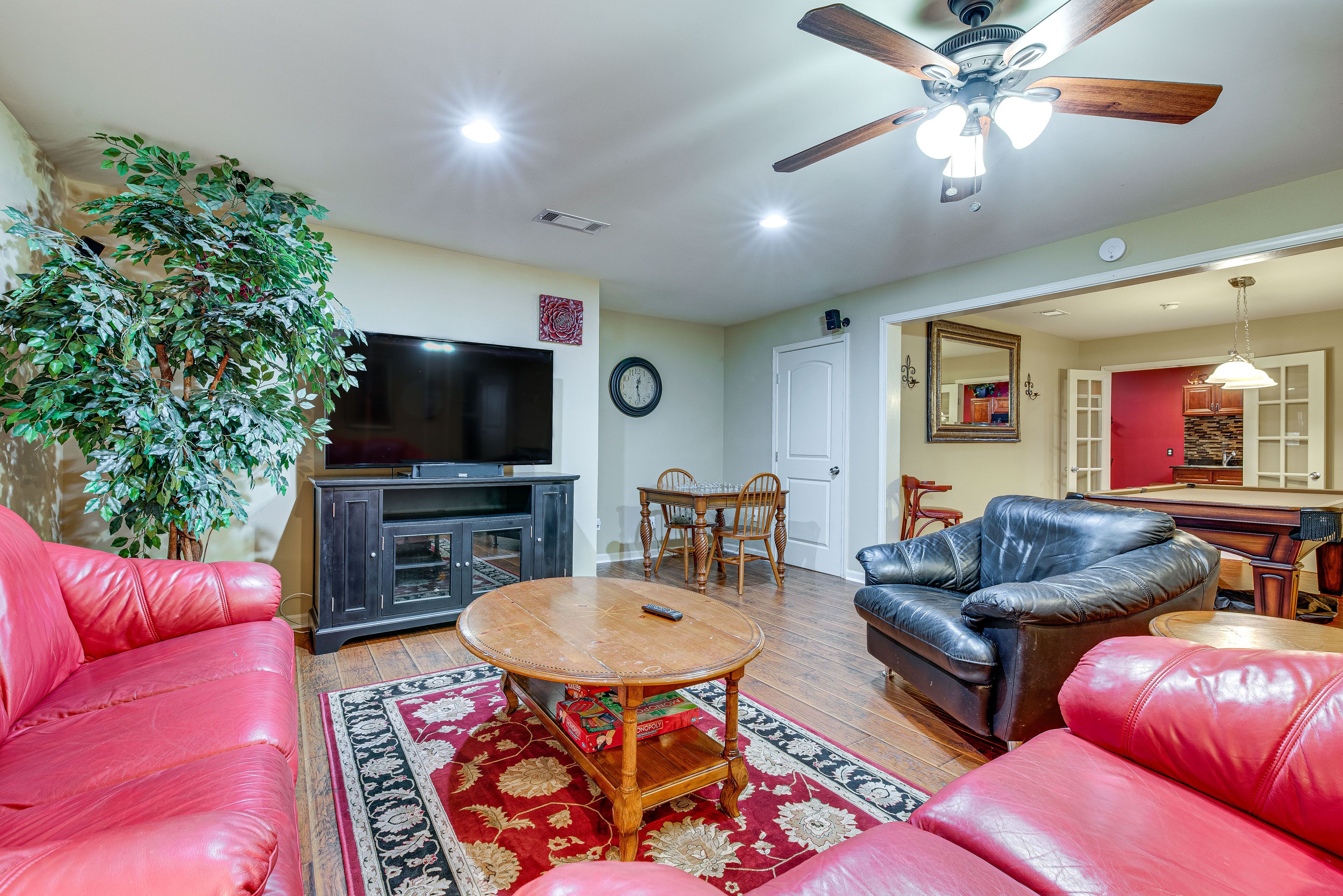 A living room with a red leather sofa, a wooden coffee table, a television, and a ceiling fan.