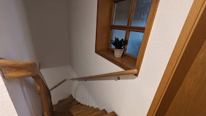 Een houten trap met een leuning, een raam met een plant en een deur onderaan.