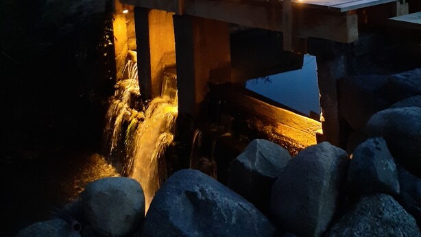 Een houten brug over een beek met een waterval, omringd door rotsen en bomen.