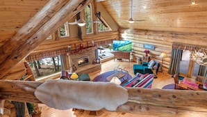 Interior de una cabaña de troncos con chimenea, televisor y zona de estar acogedora.