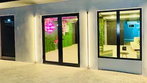 A building with a modern design, featuring large glass doors and windows, a paved entrance area, and a visible interior with furniture. - Central Boutique Hotel (Oranjestad)