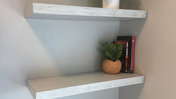 Eine Ecke mit drei weißen Regalen, auf jedem ein Topf mit einer Pflanze, ein Buch und ein zusammenrolltes Handtuch.