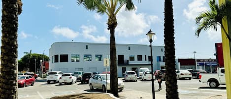 Un estacionamiento con varios coches, palmeras y un edificio de fachada blanca.