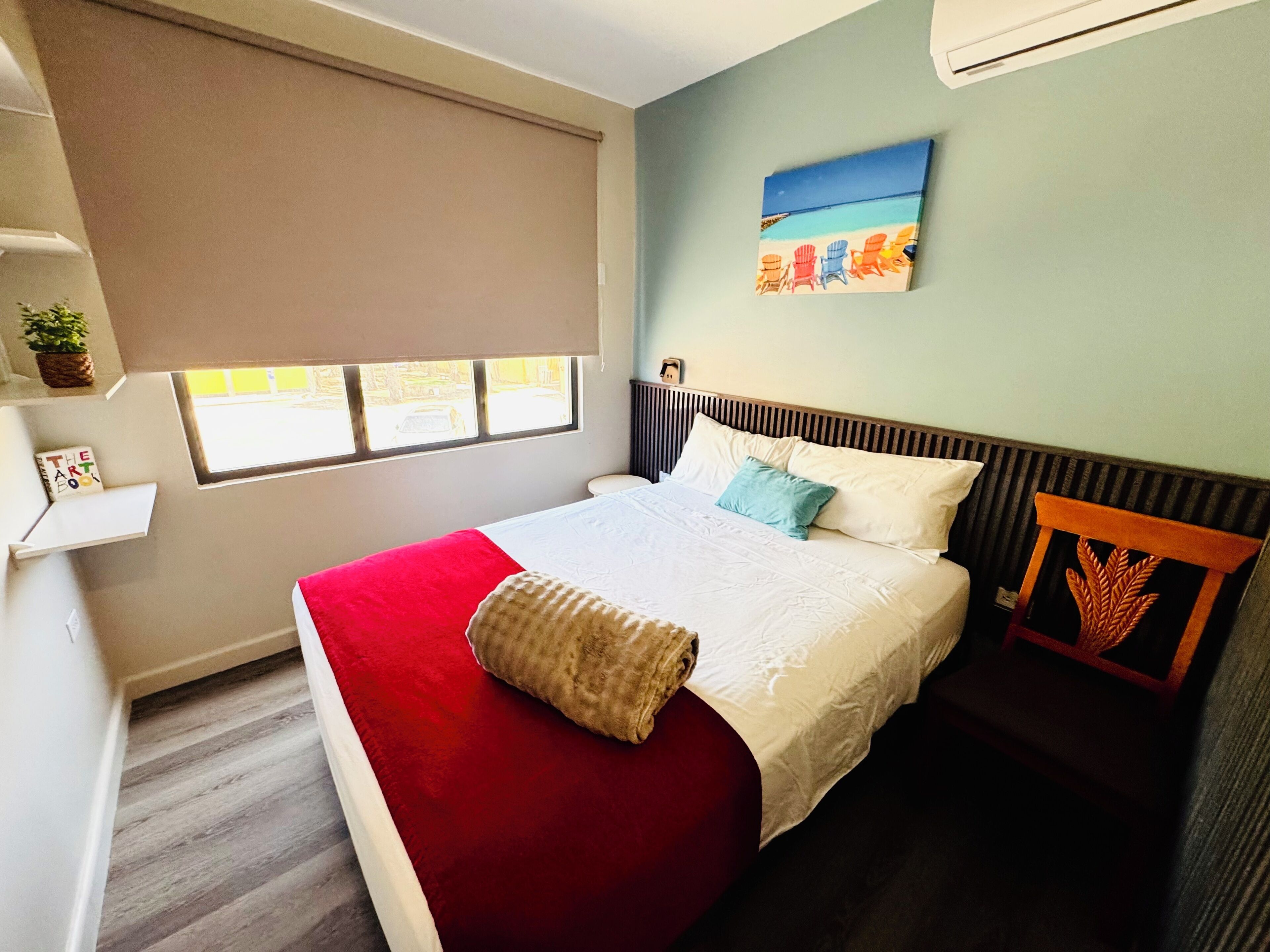 Un dormitorio con cama, ventana, un cuadro y una planta.