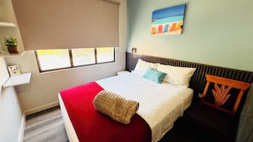 Un dormitorio con cama, ventana, un cuadro y una planta.