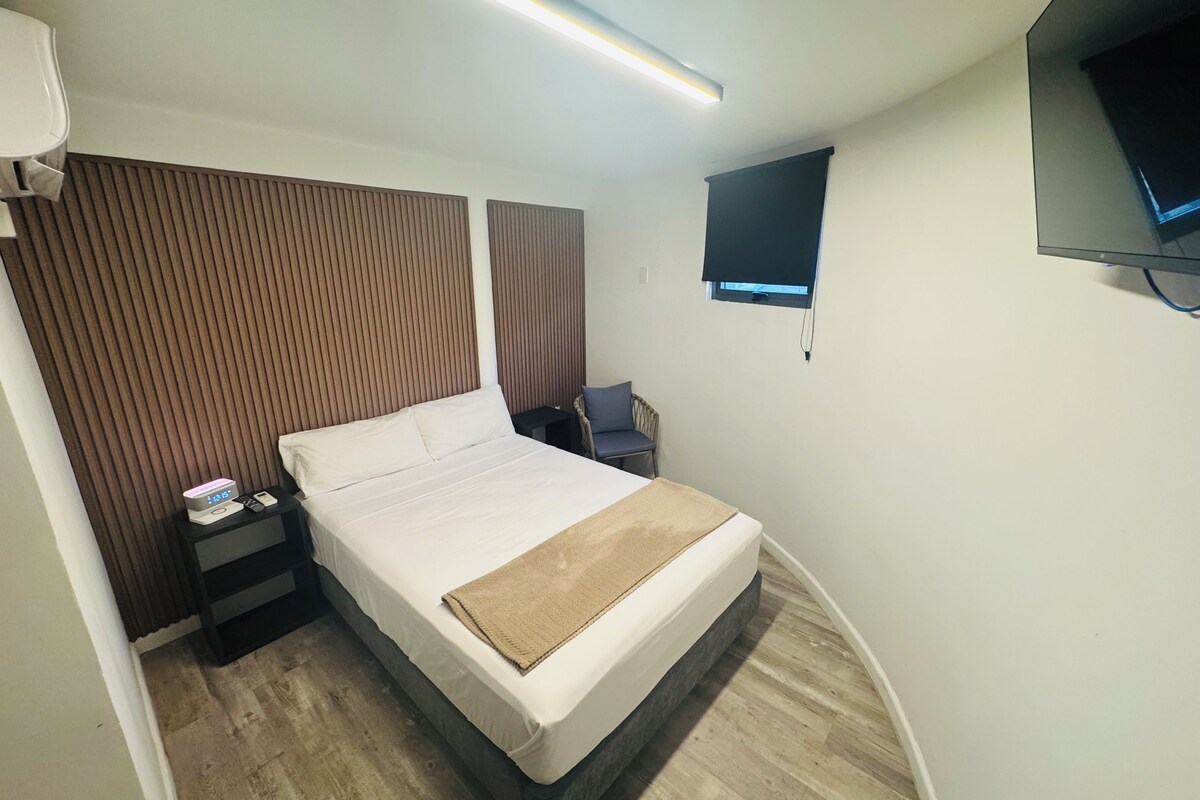 A hotel room with a bed, bedside table, TV, and a window.
