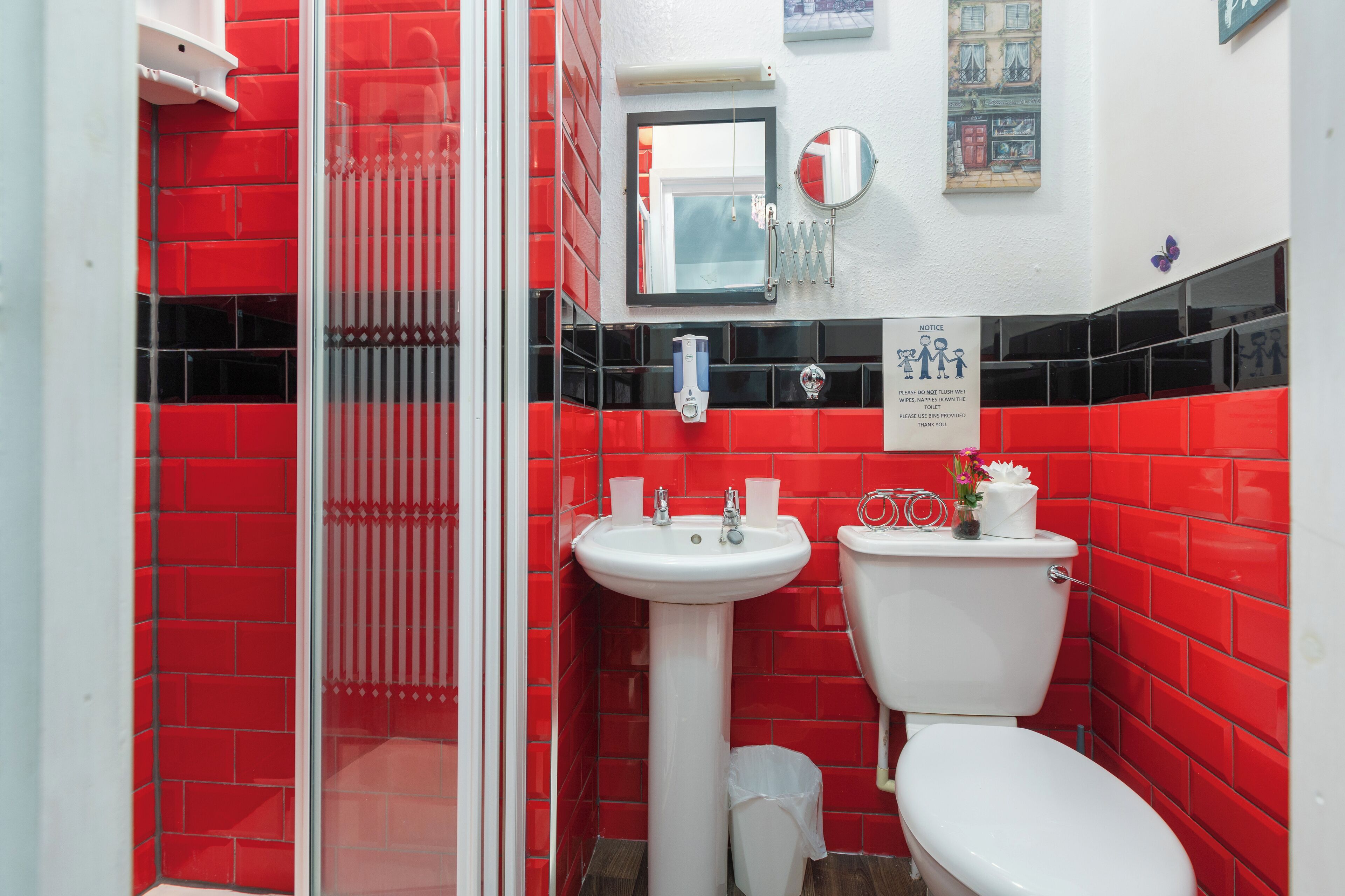 A bathroom with red tiles, a white sink, a toilet, and a glass shower enclosure.
