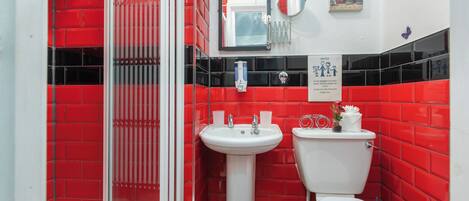 A bathroom with red tiles, a white sink, a toilet, and a glass shower enclosure.
