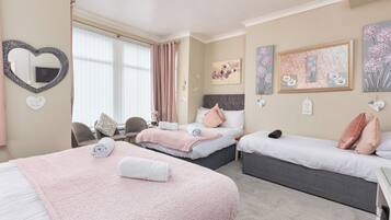 A hotel room with two beds, a heart-shaped mirror, floral artwork, and a small table with chairs.