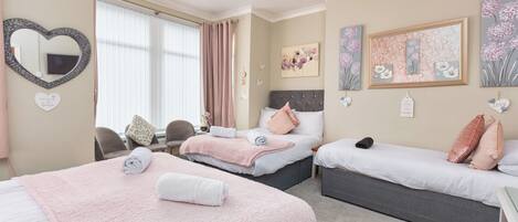 Habitación de hotel con dos camas, un espejo con forma de corazón, obra de arte floral y una pequeña mesa con sillas.