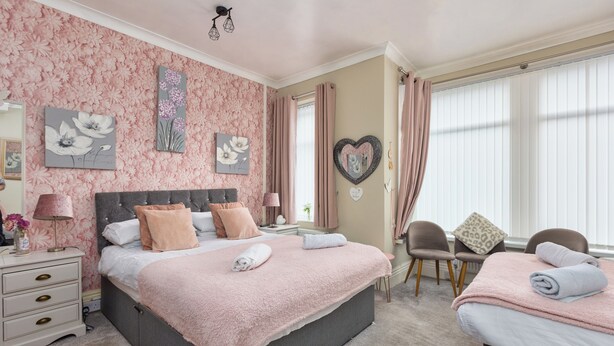 A bedroom with a large bed, bedside tables, a chair, and a small table. - Friends Hotel (Blackpool)
