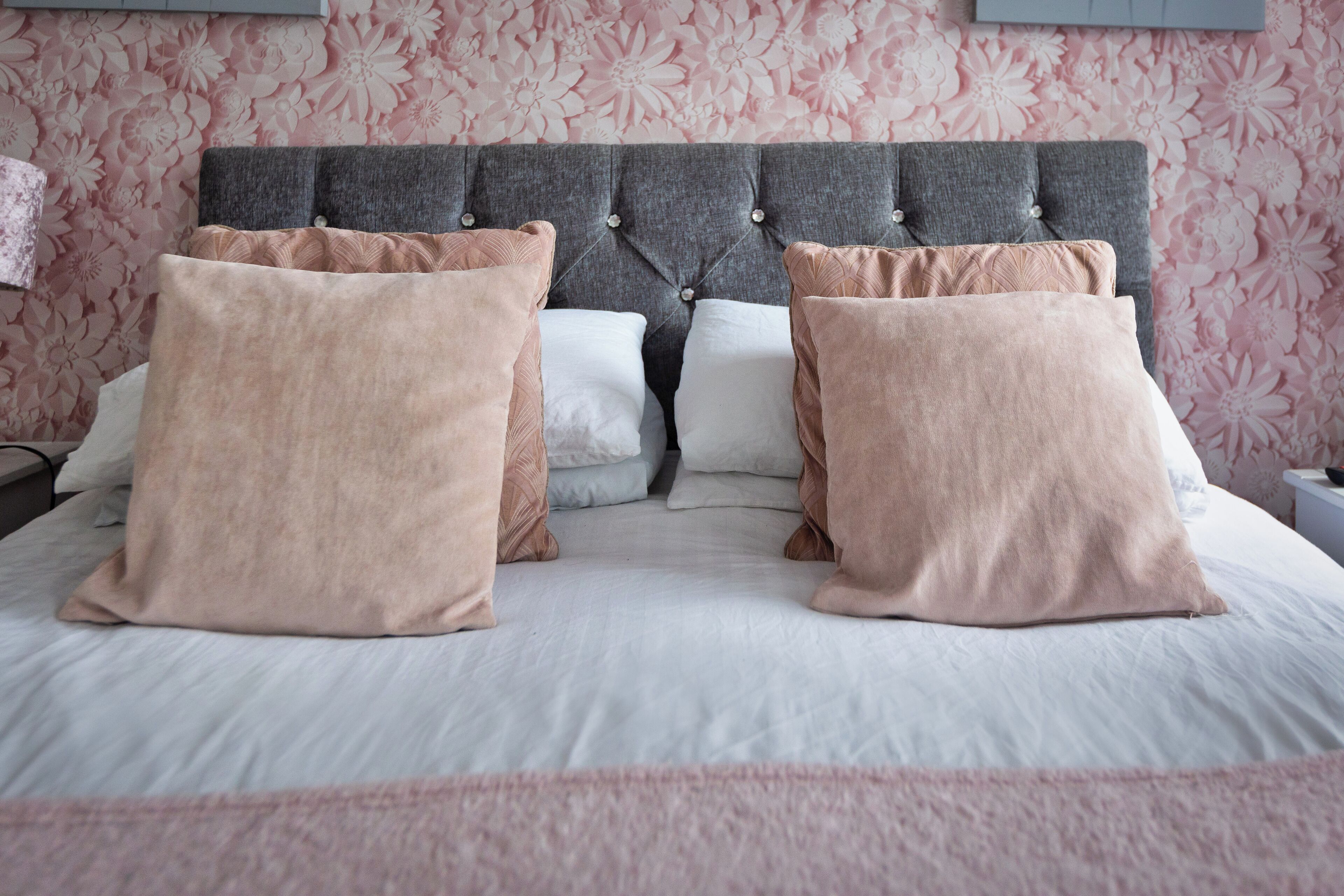 A neatly made bed with a grey tufted headboard and pink and white pillows.