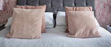 A neatly made bed with a grey tufted headboard and pink and white pillows.