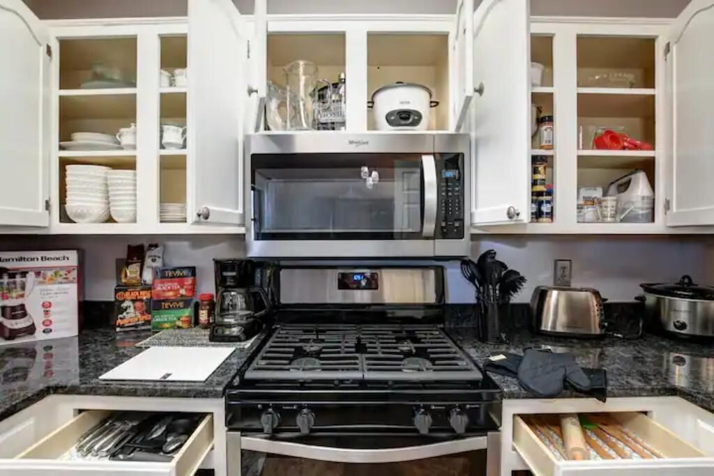 A kitchen with white cabinets, a microwave, a stove, and various kitchen utensils.