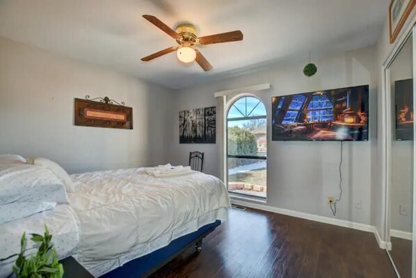 Una camera da letto con un letto, una ventola a soffitto, una finestra e una TV a parete.