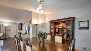 Un comedor con mesa y sillas de madera, una araña y un aparador con puertas de cristal.