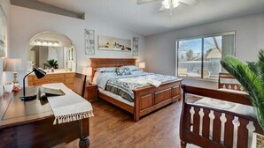 Un dormitorio con una cama de madera, un escritorio con lámpara, un espejo y un ventilador de techo.