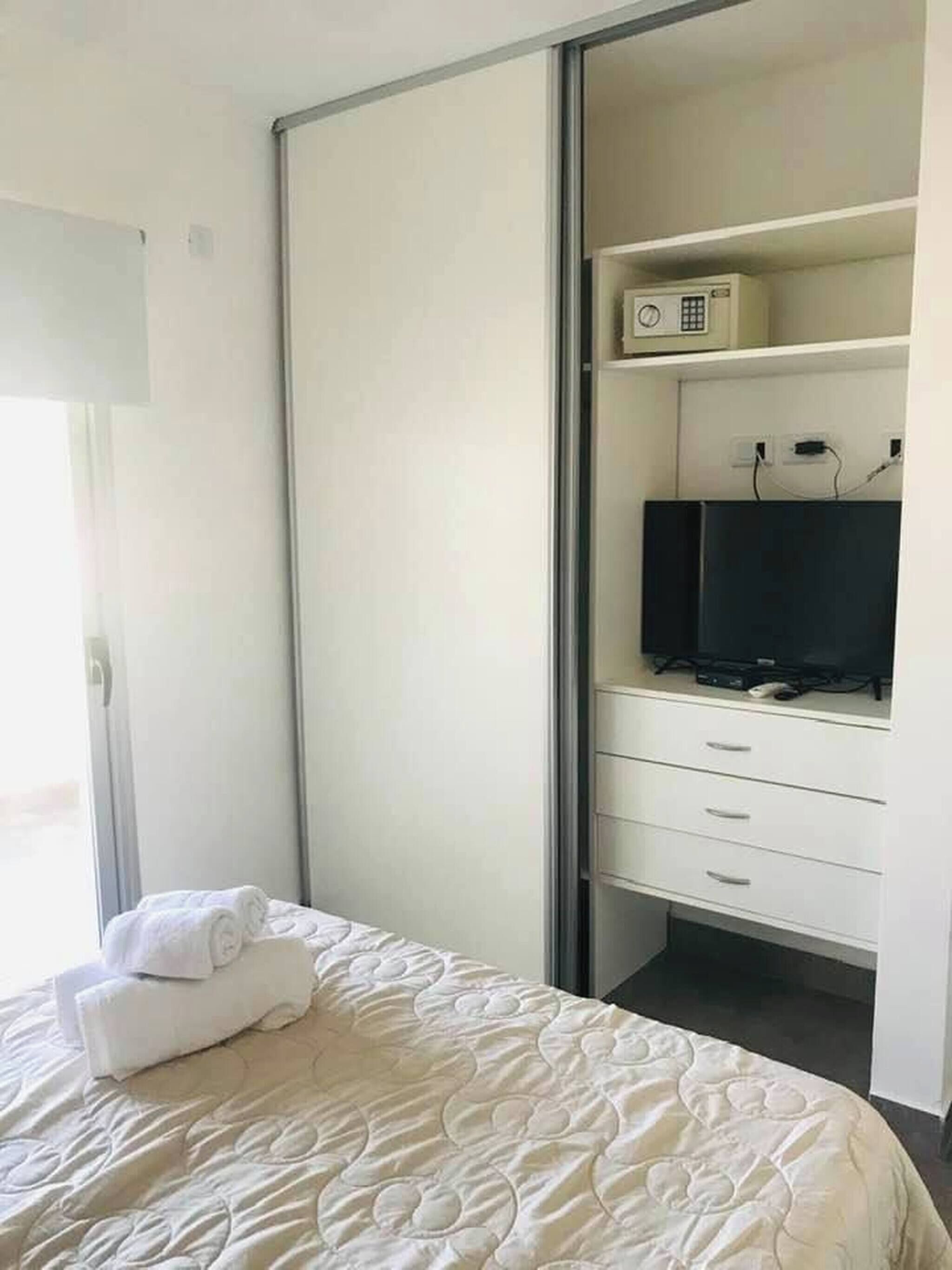 Un dormitorio con cama, armario, televisor y ventana.