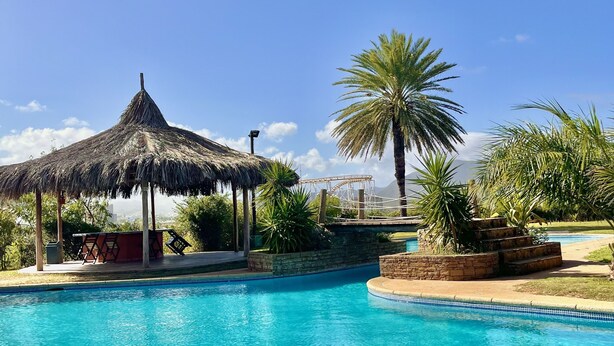 A clear blue swimming pool with a thatched-roof gazebo and palm trees in the background. - Stay at Casa Carnaval walking distance to Playa Moreno (Pampatar)