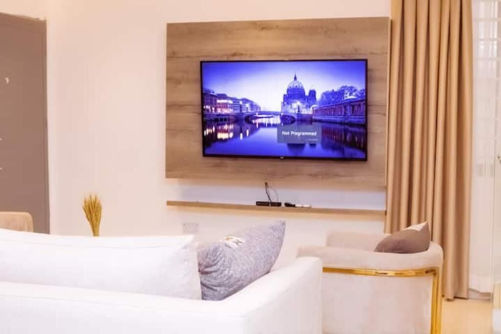 Uma sala de estar moderna com uma TV de tela plana na parede, um sofá branco e uma mesinha.
