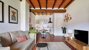 Una sala de estar con un sofá, una mesa de centro y un mueble para televisión. En el fondo, se ve una cocina con armarios y un comedor.