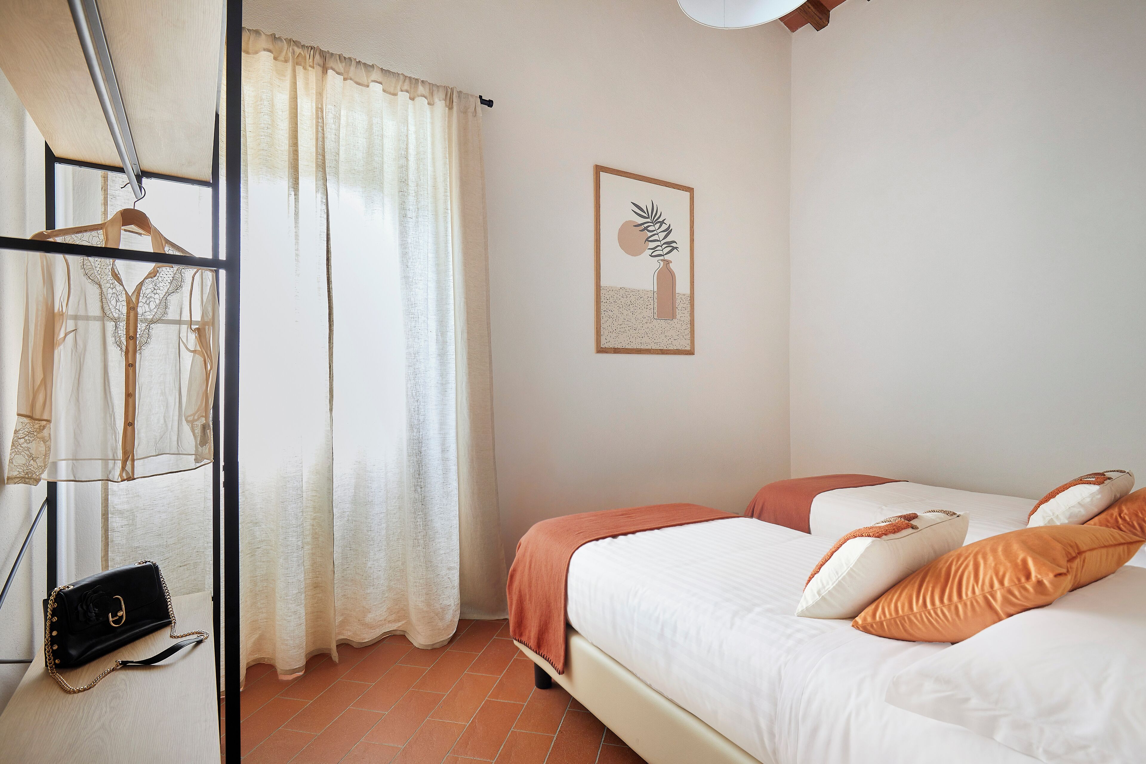 A bedroom with a bed, a hanging garment rack, and a framed picture on the wall.
